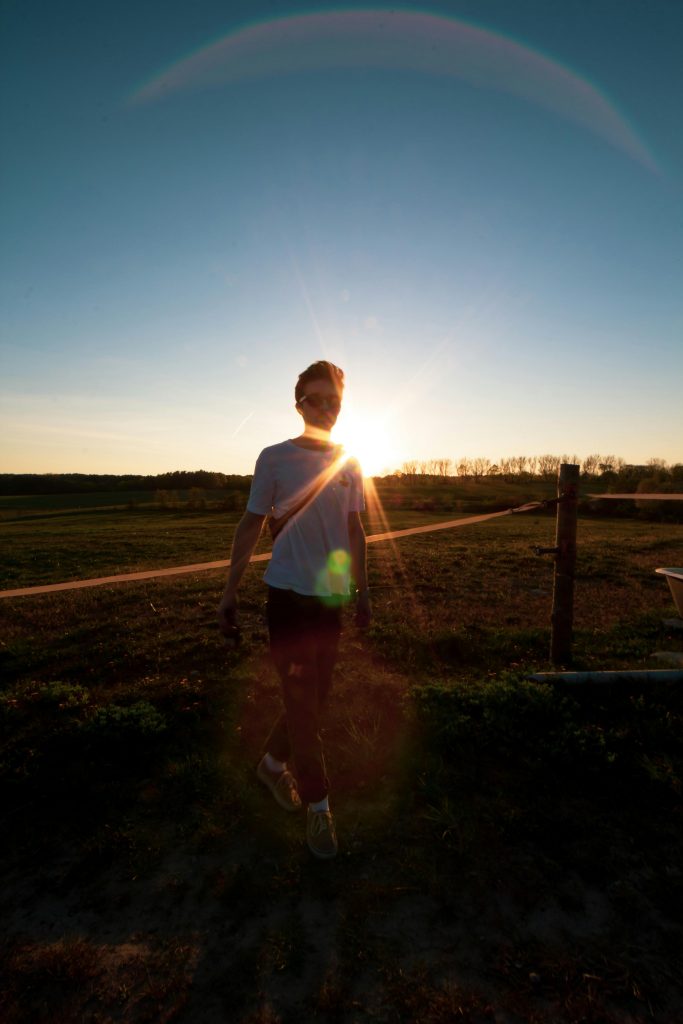 pexels photo 2931775 2931775 A man walks outdoors in Rheinsberg at sunset, casting a striking silhouette against the sun.